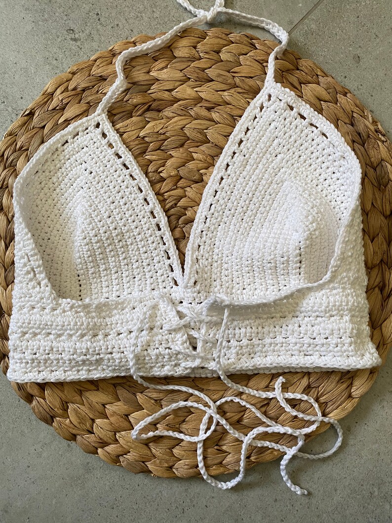 May include: White crocheted halter top with a lace-up front. The top is made with a delicate stitch and has a relaxed fit.