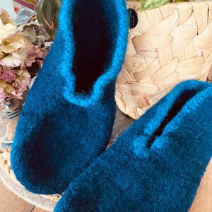 May include: A pair of dark blue wool slippers with a contrasting blue trim. The slippers are on a wooden surface and the text "NACHTBLAU / PETROL" is visible in the background.