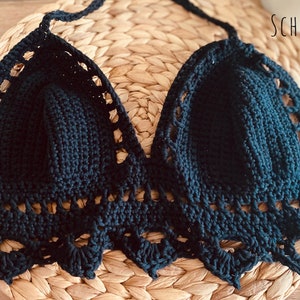Peut inclure: Haut de bikini noir fait &agrave; la main, crochet&eacute;, avec un col halter et une bordure festonn&eacute;e. Le haut est fait d'un fil sombre et est pr&eacute;sent&eacute; sur une surface tiss&eacute;e. Le mot "SCHWARZ" est visible.