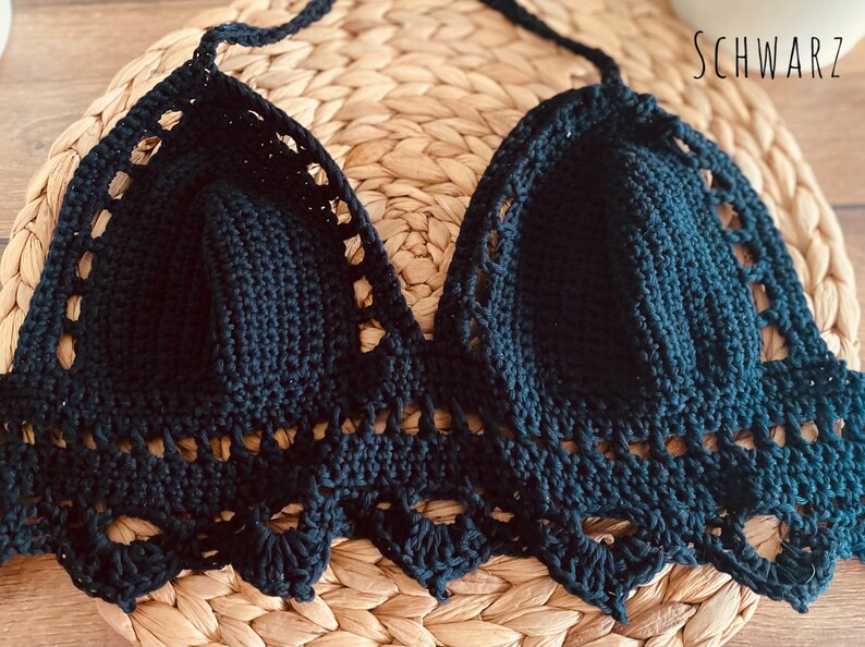 Peut inclure: Haut de bikini noir fait &agrave; la main, crochet&eacute;, avec un col halter et une bordure festonn&eacute;e. Le haut est fait d'un fil sombre et est pr&eacute;sent&eacute; sur une surface tiss&eacute;e. Le mot "SCHWARZ" est visible.