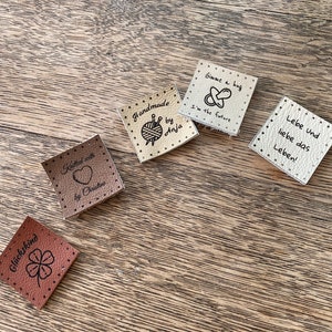 May include: Five different leather labels with various designs and text. The labels are beige and brown. The text on the labels includes "Knitted with love by Christine", "Handmade by Anja", "Gimme a hug I'm the future", "Gl&uuml;ckskind" and "Lebe und liebe das Leben!"