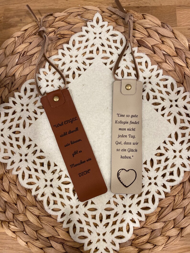 May include: Two leather bookmarks with inspirational quotes. The brown bookmark says "Weil Engel nicht &uuml;berall sein k&ouml;nnen, gibt es Menschen wie DICH". The beige bookmark says "Eine so gute Kollegin findet man nicht jeden Tag. Gut, dass wir so ein Gl&uuml;ck haben."