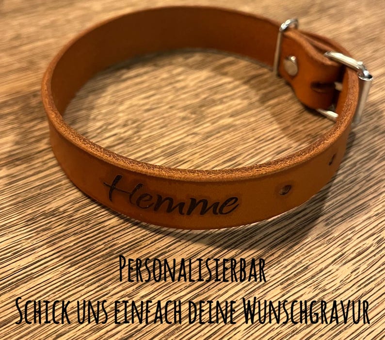 Op de afbeelding: Een bruine leren hondenriem met het woord "Hemme" erop gegraveerd. De riem is gepersonaliseerd en je kunt je eigen tekst toevoegen.