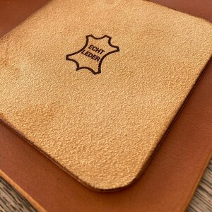 May include: A light brown leather coaster with the text "Echt Leder" in a black oval.