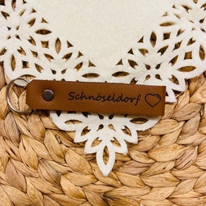 May include: Brown leather keychain with a silver key ring and the text "Schn&ouml;seldorf" with a small heart.
