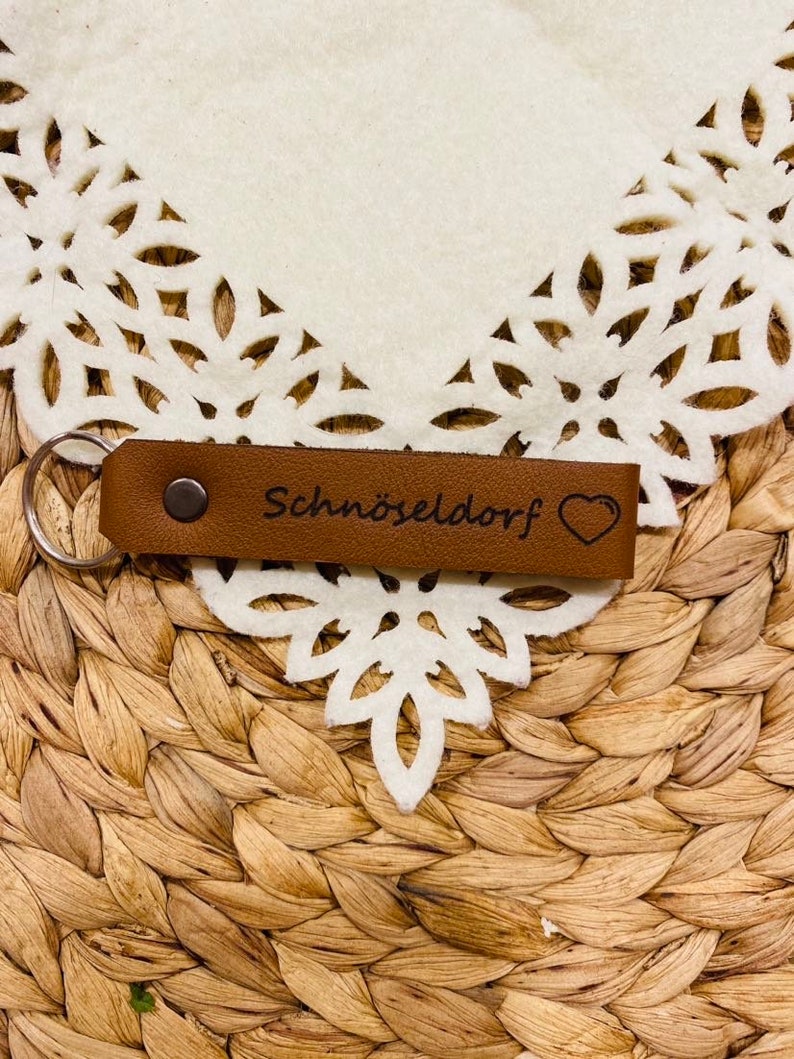 May include: Brown leather keychain with a silver key ring and the text "Schn&ouml;seldorf" with a small heart.