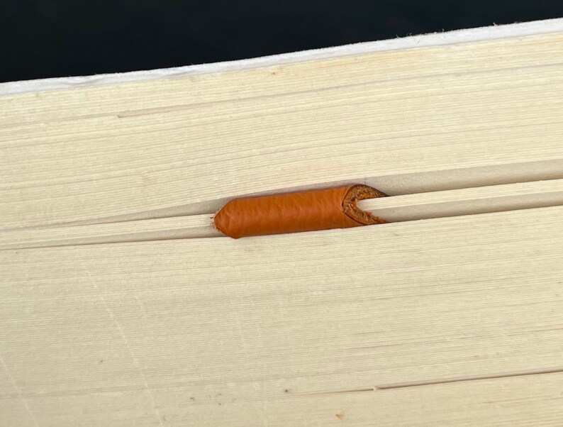 Peut inclure: Une surface en bois clair pr&eacute;sentant une rainure horizontale avec un petit insert cylindrique en cuir orange-brun plac&eacute; au centre du canal. Le grain du bois est visible et la pi&egrave;ce en cuir pr&eacute;sente une texture lisse et arrondie.