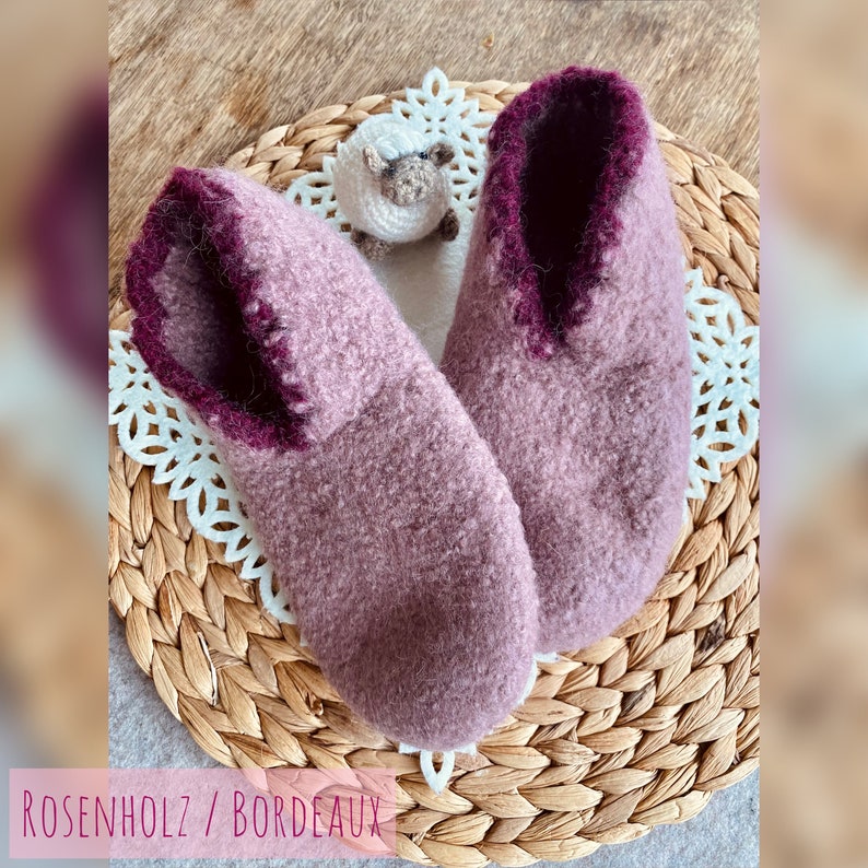 May include: A pair of soft, fuzzy slippers in a light purple color with a burgundy trim. The slippers are sitting on a woven wicker basket with a white doily.