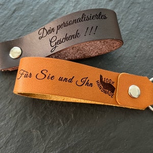 May include: Two leather keychains with engraved text. The top keychain is brown and says "Dein personalisiertes Geschenk!!!". The bottom keychain is tan and says "F&uuml;r Sie und Ihn 100% HANDMADE".