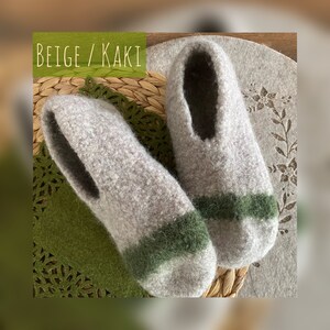 May include: Beige and green wool slippers with a contrasting stripe. The slippers are on a woven mat.