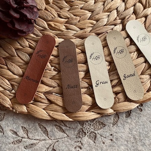 May include: Five leather swatches with different colors and names: Marone, Nuss, Grau, Sand, Creme. Each swatch has a small circle with the letters "HB" inside.