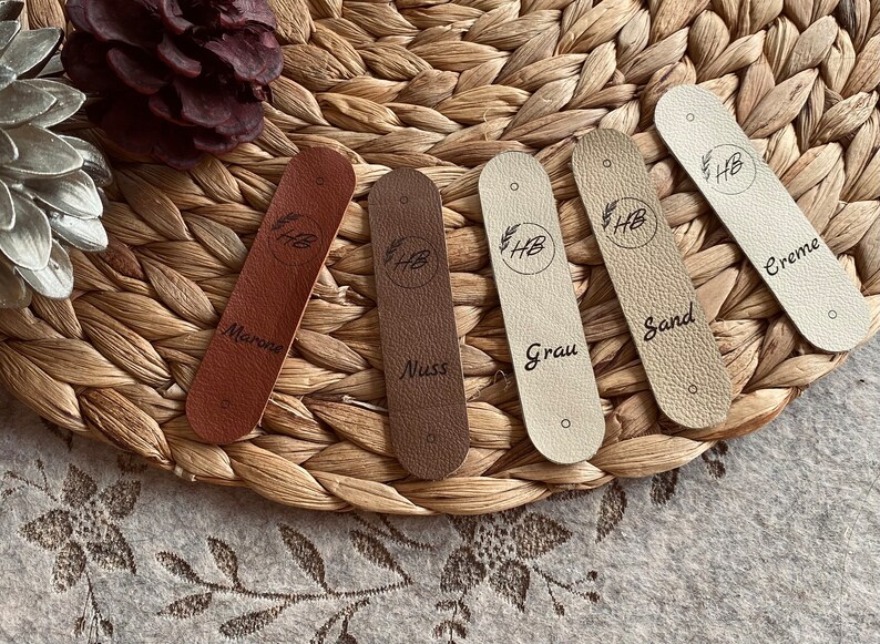 May include: Five leather swatches with different colors and names: Marone, Nuss, Grau, Sand, Creme. Each swatch has a small circle with the letters "HB" inside.