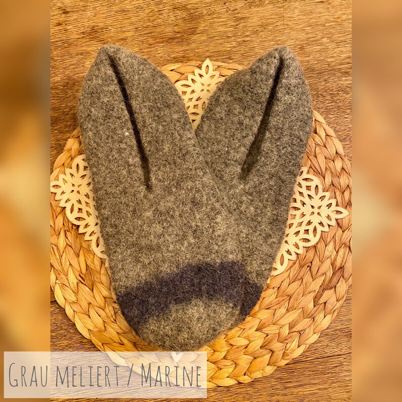 May include: A pair of gray and navy blue wool slippers with a textured surface. The slippers are on a woven wicker mat.