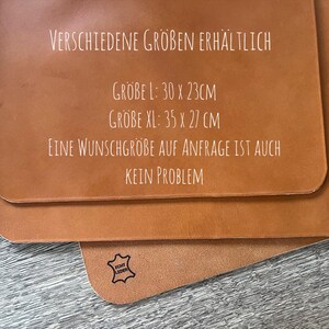 May include: A close-up of a brown leather surface with white text that reads "VERSCHIEDENE GR&Ouml;BEN ERH&Auml;LTLICH" and lists sizes in centimeters: "GROBE L: 30 X 23CM", "GROBE XL: 35 X 27 CM". The text continues: "EINE WUNSCHGROBE AUF ANFRAGE IST AUCH KEIN PROBLEM". A small black stamp with the text "ECHT LEDER" is visible in the lower right corner.