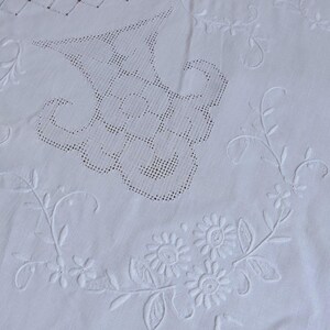 May include: White embroidered tablecloth with floral and geometric patterns. The design includes detailed floral arrangements, delicate vines, and openwork sections. The cloth is made of a soft, white fabric, perfect for a dining table.