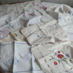 Puede incluir: Una colección de ropa de cama vintage blanca, que incluye manteles y servilletas, con diseños florales bordados en varios colores. Algunas piezas presentan adornos de encaje y patrones geométricos. Se puede ver una variedad de tamaños y estilos.