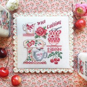 Op de afbeelding: Een witte kruissteekborduursel met een rood en wit keukenthema. De borduursel toont een mixer, een kan, een kom en kersen. De tekst "Avec Cuisine Digoin" is in rood geborduurd.