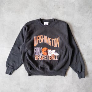 May include: A black crew neck sweatshirt with the words "WASHINGTON GIRLS BASKETBALL" in orange lettering. A basketball and a pair of trainers are also featured in the design. The sweatshirt is a vintage style.