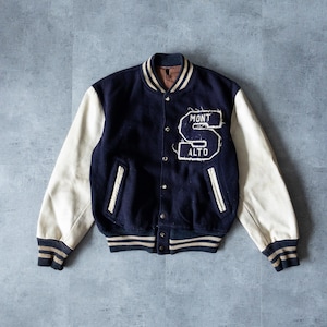 Puede incluir: Una chaqueta de béisbol vintage azul marino y blanca con un gran parche de letras "MONT ALTO" en el pecho. La chaqueta tiene una manga de cuero blanco y un cuello, puños y cintura de punto de canalé.