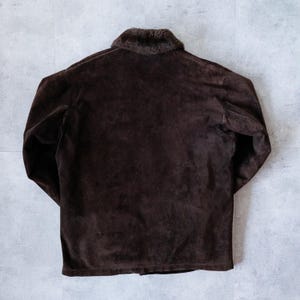 K&ouml;nnte beinhalten: Dunkelbraune Wildlederjacke mit Kunstfellkragen. Die Jacke hat lange &Auml;rmel und einen Knopfverschluss. Die R&uuml;ckseite der Jacke ist sichtbar und zeigt die Textur des Wildledermaterials. Die Jacke ist ein klassischer Stil.