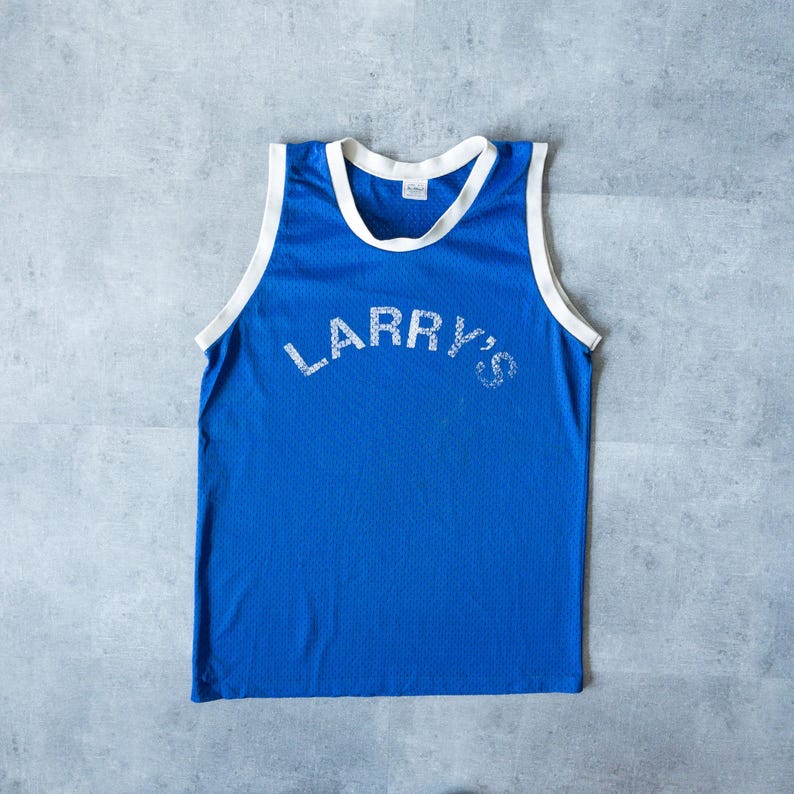 May include: A blue mesh tank top with white trim around the neck and armholes. The text "LARRY'S" is printed across the chest in white, distressed lettering. The tank top is sleeveless and has a classic athletic style.