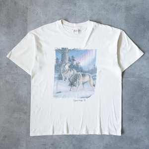 May include: Off-white t-shirt featuring a graphic of two wolves in a snowy forest under a colorful sky. The text "Pigeon Forge TN" is printed below the image. The shirt has a crew neck and short sleeves.