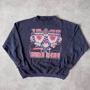 May include: Navy blue sweatshirt with a graphic design commemorating the 1995 World Series. The design includes the text "Braves vs. Indians" and team logos. The sweatshirt has long sleeves and a crew neck.