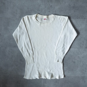 Peut inclure: T-shirt thermique blanc cassé à manches longues, col rond et poignets côtelés. Le t-shirt présente une texture gaufrée et une petite étiquette rouge et blanche près de l'encolure. L'ourlet inférieur est légèrement froncé.