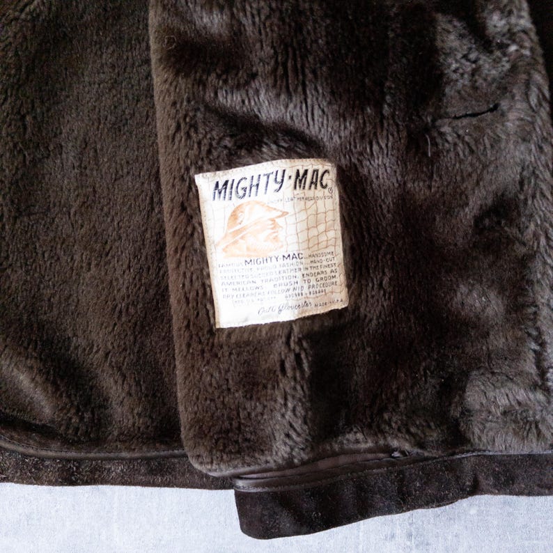 K&ouml;nnte beinhalten: Nahaufnahme des Innenraums einer braunen Mighty-Mac-Jacke. Das weiche, dunkelbraune Futter kontrastiert mit dem Etikett, das den Markennamen und eine Grafik eines Hutes zeigt. Das Etikett enth&auml;lt Details &uuml;ber die Konstruktion der Jacke.