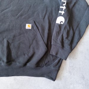 Puede incluir: Sudadera con capucha negra con bolsillo de canguro y un peque&ntilde;o logotipo cuadrado en la parte delantera. La manga izquierda presenta texto blanco y un logotipo blanco. La sudadera est&aacute; hecha de un material suave y c&oacute;modo.