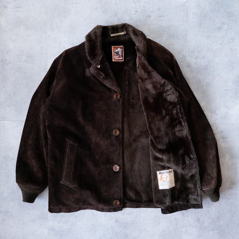 K&ouml;nnte beinhalten: Braune Jacke mit Kn&ouml;pfen, Kunstfellfutter und Kragen. Die Jacke hat ein klassisches Design mit einem Etikett innen. Die Jacke hat ein weiches, strukturiertes Aussehen und einen warmen Look.