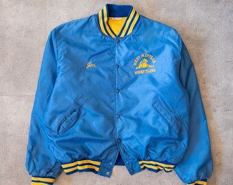 May include: A blue satin jacket with a yellow and blue striped collar, cuffs, and waistband. The jacket features the name "Jim" embroidered on the chest and "West Mifflin Wrestling" on the back.
