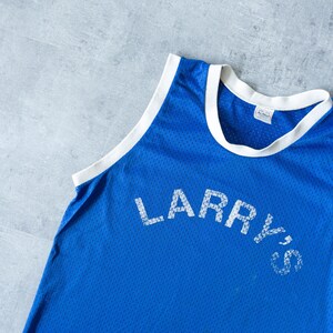 May include: A blue mesh tank top with white trim around the neckline and armholes. The text "LARRY'S" is printed across the front in white. The tank top is made of a breathable material.
