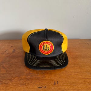 May include: A black and yellow baseball cap with a curved peak. The front of the cap features a circular logo with the text "CATALYTIC Enterprises Limited" in red and white.