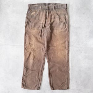 Puede incluir: Pantalones de pana marrones con un dise&ntilde;o cl&aacute;sico de cinco bolsillos. Los pantalones tienen un aspecto descolorido y un corte recto. La tela parece ser una pana de peso medio, adecuada para ropa informal. Los pantalones est&aacute;n colocados sobre una superficie clara.