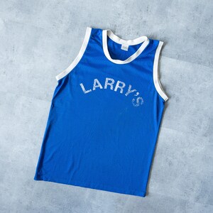 May include: A blue mesh tank top with white trim around the collar and armholes. The text "LARRY'S" is printed across the chest in white lettering. The tank top is a vintage athletic style.