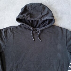 Puede incluir: Una sudadera con capucha negra con cord&oacute;n y capucha forrada. La sudadera tiene un bolsillo tipo canguro y pu&ntilde;os y dobladillo acanalados. La tela parece ser un material suave de peso medio.