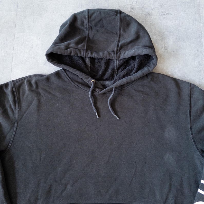 Puede incluir: Una sudadera con capucha negra con cord&oacute;n y capucha forrada. La sudadera tiene un bolsillo tipo canguro y pu&ntilde;os y dobladillo acanalados. La tela parece ser un material suave de peso medio.