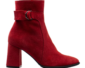 May include: Red suede ankle boots with a block heel and a buckle detail on the ankle strap.