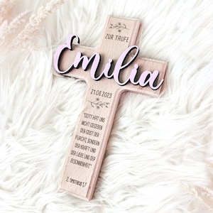 May include: A wooden cross with the name "Emilia" in pink lettering, the date "21.08.2023", and the text "Zur Taufe" (German for "For Baptism"). The cross also features a Bible verse from 2 Timothy 1:7.