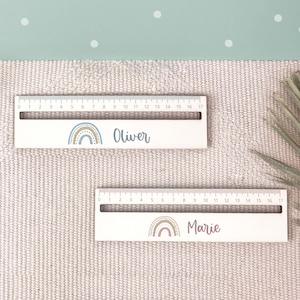 May include: Two wooden rulers with rainbow designs and personalized names. The top ruler says "Oliver" and the bottom ruler says "Marie".