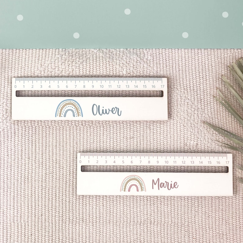 May include: Two wooden rulers with rainbow designs and personalized names. The top ruler says "Oliver" and the bottom ruler says "Marie".