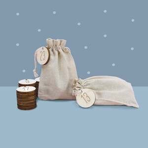 May include: A set of wooden Christmas advent calendar numbers in a burlap sack. The numbers are 9, 13, 17, and 23. The sack is beige and has a drawstring closure.
