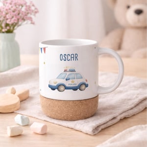 May include: White ceramic mug with a cork base, featuring the name "OSCAR" and a cartoon police car illustration. The car is white and blue with the word "Polizei" on the side. The mug has a white handle and is decorated with small stars.