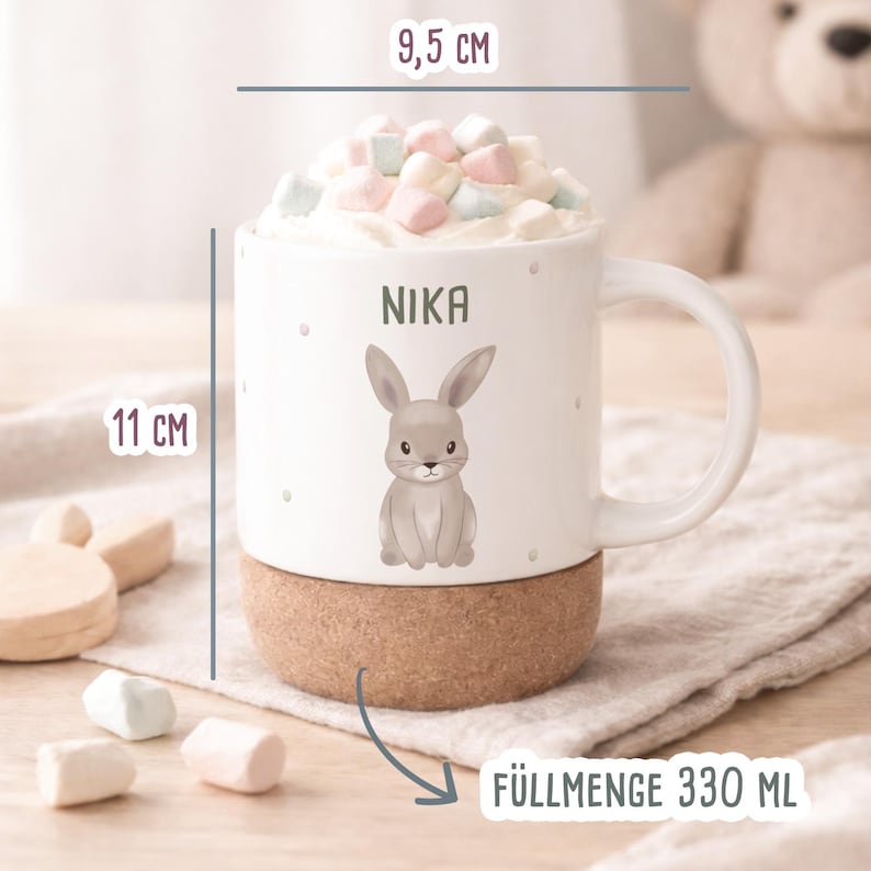 May include: A white ceramic mug with a cork base, 4.3 inches tall and 3.7 inches wide, featuring a gray bunny illustration and the name "NIKA". The mug is filled with marshmallows and has a capacity of 11.1 fluid ounces.
