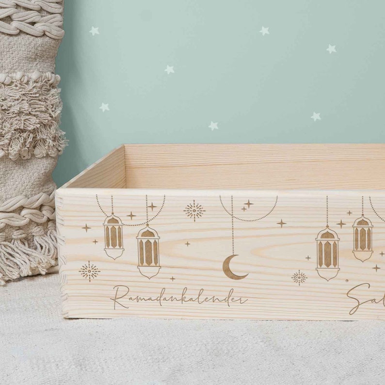 May include: A wooden box with a Ramadan calendar design. The box is decorated with stars, crescent moons, and lanterns. The text "Ramadankalender" is engraved on the box.