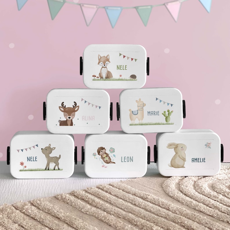 K&ouml;nnte beinhalten: F&uuml;nf wei&szlig;e Lunchboxen mit bunten Tierillustrationen und Namen. Die Lunchboxen haben schwarze Griffe und sind pyramidenf&ouml;rmig gestapelt.