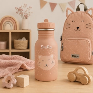 Peut inclure: Une gourde en métal rose poudré ornée d'une illustration de visage de chat blanc et du prénom Emilia imprimé en lettres blanches. La bouteille possède un bouchon à vis assorti avec une petite anse et un motif de petits points blancs sur le bas.