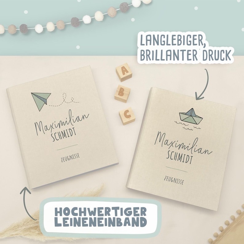 May include: Two beige linen-covered folders with the name Maximilian Schmidt and the word Zeugnisse printed on the front. One folder features a paper airplane graphic, and the other shows a paper boat. Text bubbles read Langlebiger, brillanter Druck.