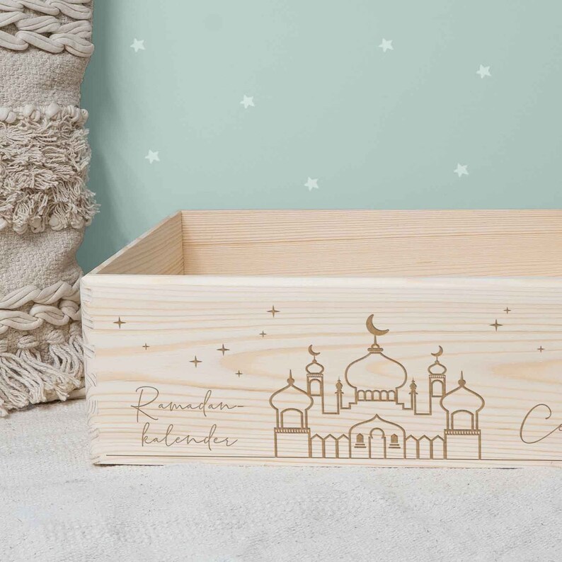 May include: A wooden box with a Ramadan calendar design. The box is decorated with a mosque silhouette, stars, and the words "Ramadan kalender".